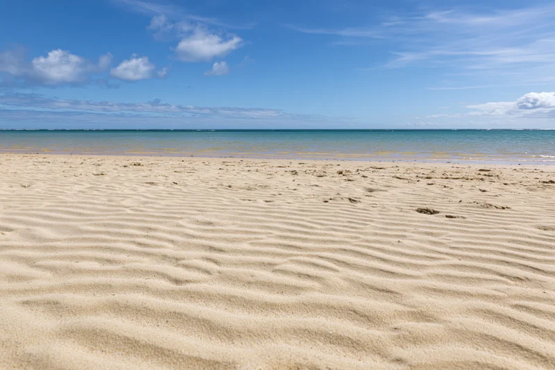 Rippled golden sand on a tropical beach under a clear blue sky with scattered clouds