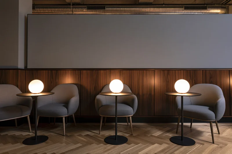 Three gray armchairs with round tables and spherical lamps arranged in a modern cafe interior with wood paneling and herringbone flooring
