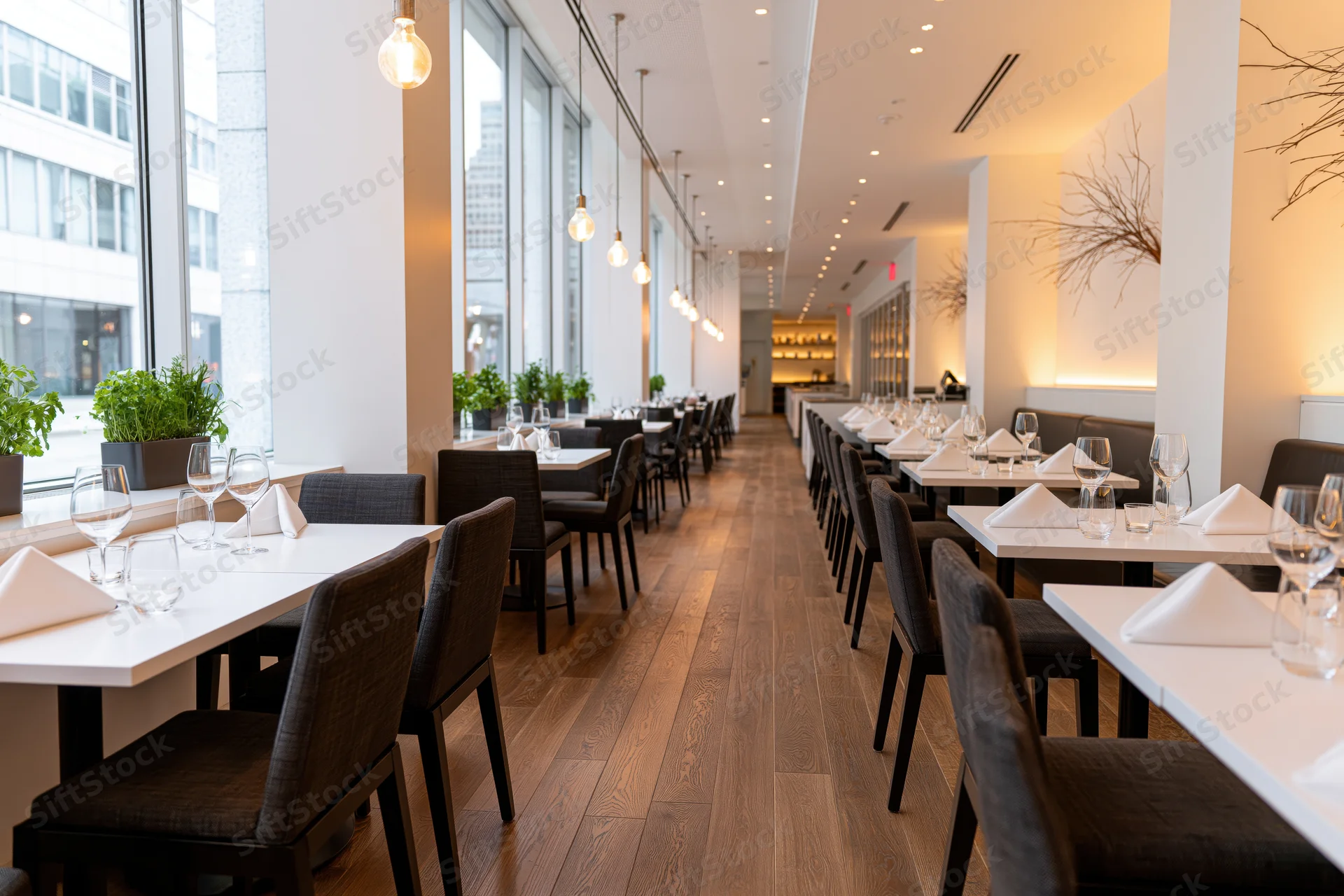 Empty upscale restaurant dining room with tables set for service along a wooden floor near large windows