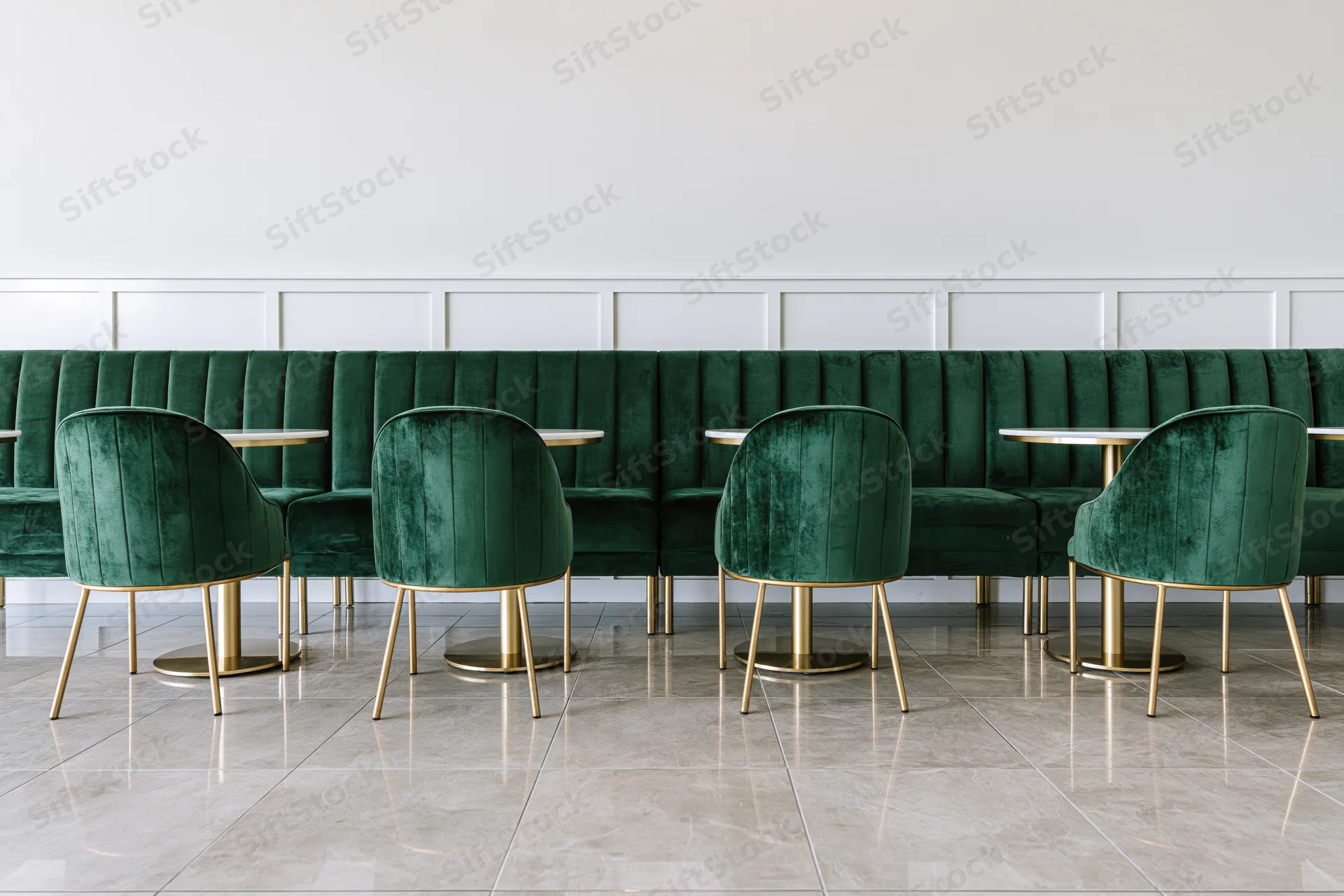 Row of emerald velvet chairs with gold legs arranged along a white paneled booth in a modern restaurant interior