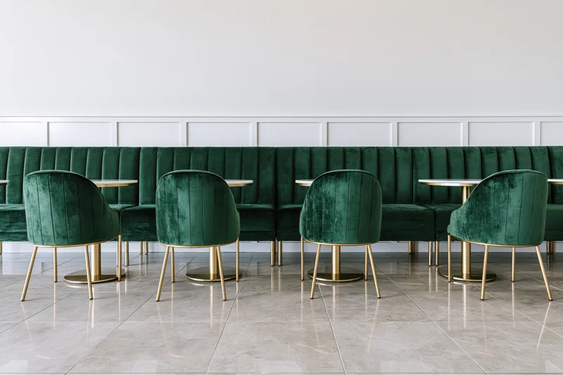 Row of emerald velvet chairs with gold legs arranged along a white paneled booth in a modern restaurant interior