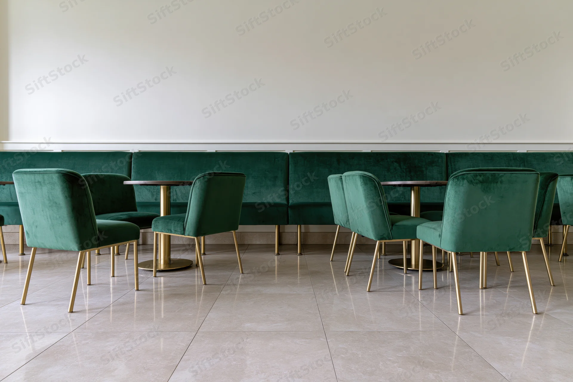 Empty upscale restaurant interior with emerald velvet chairs and gold legs arranged along a white wall with marble flooring