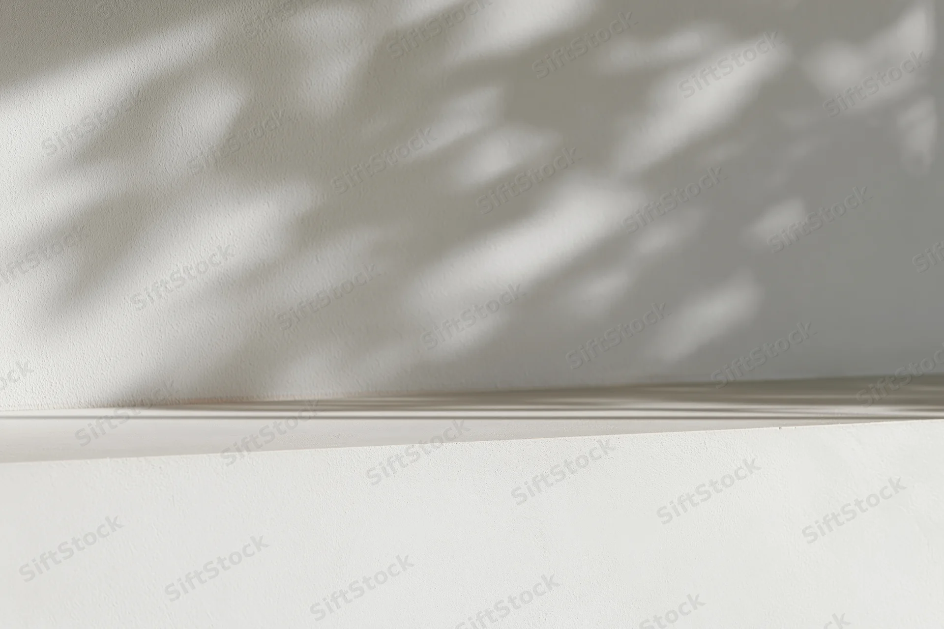 Dappled leaf shadows on a white concrete wall in an interior space