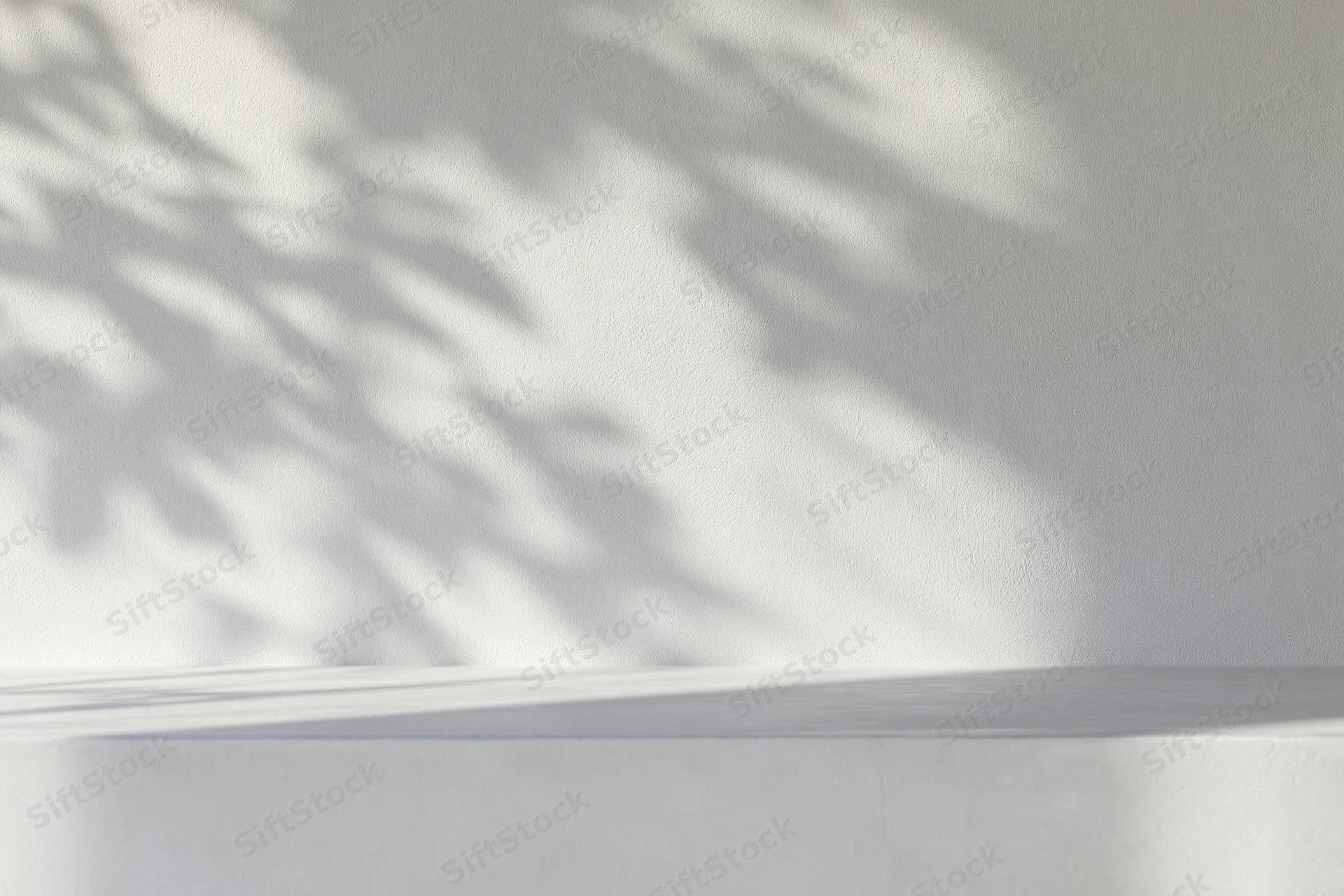 White concrete wall with dappled leaf shadows and empty shelf in minimalist interior