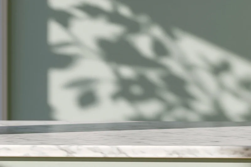 White marble surface with leaf shadows on a green wall in a modern interior