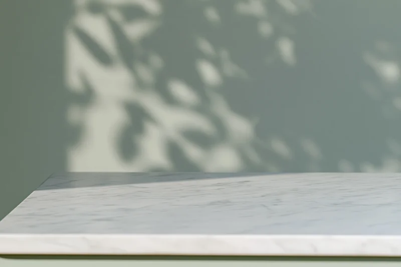 White marble surface with leaf shadows on green wall, copyspace for product display