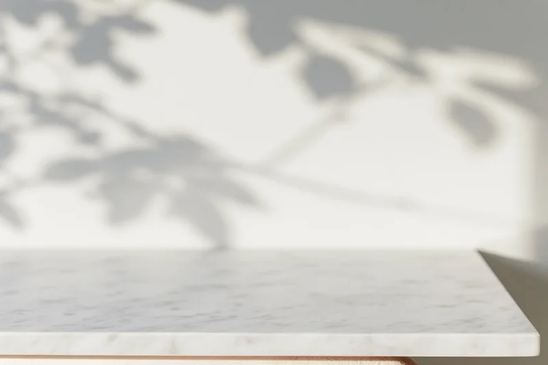 White marble tabletop with leaf shadows on a light wall, smooth surface in a modern interior