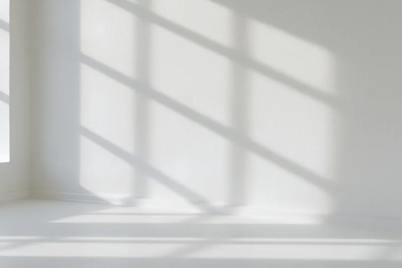 Empty white room interior with window shadow patterns on walls and floor