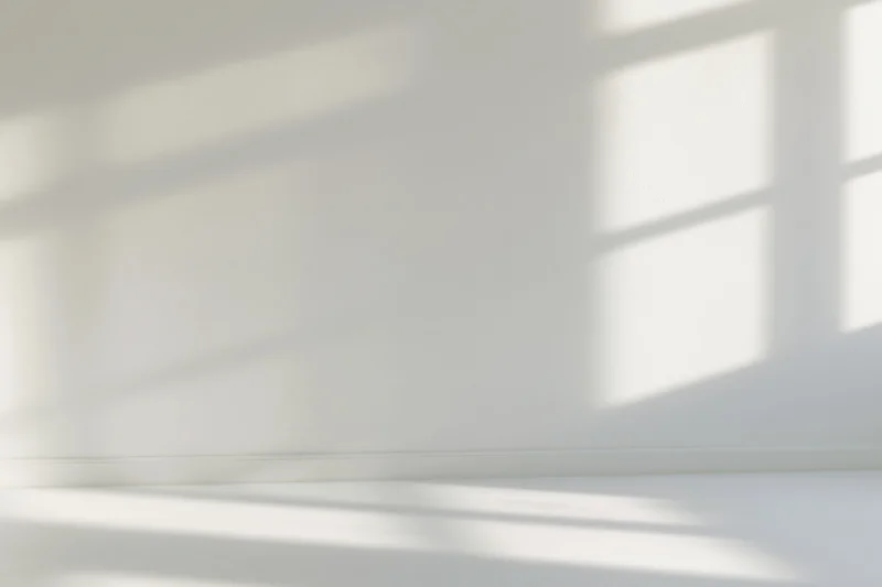 Empty white room interior with soft window shadow patterns on walls and floor