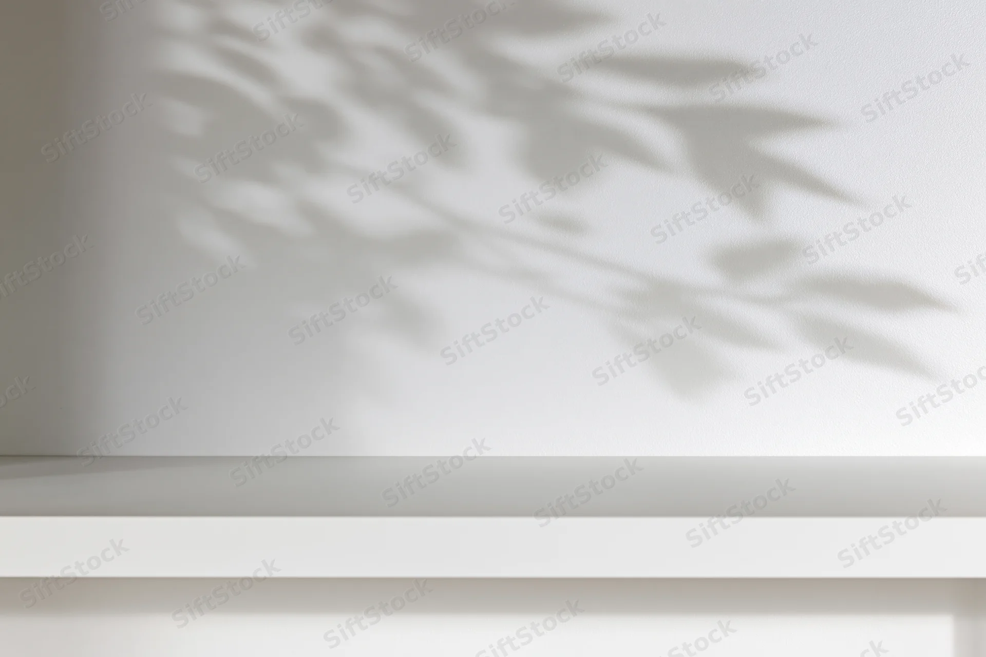 Empty white shelf against a plain wall with soft leaf shadows