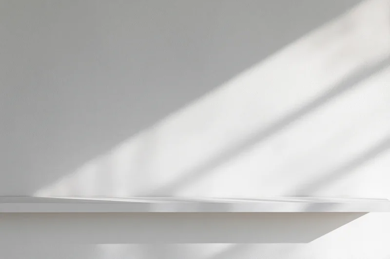 Empty white shelf mounted on a smooth white wall in a minimalist studio space