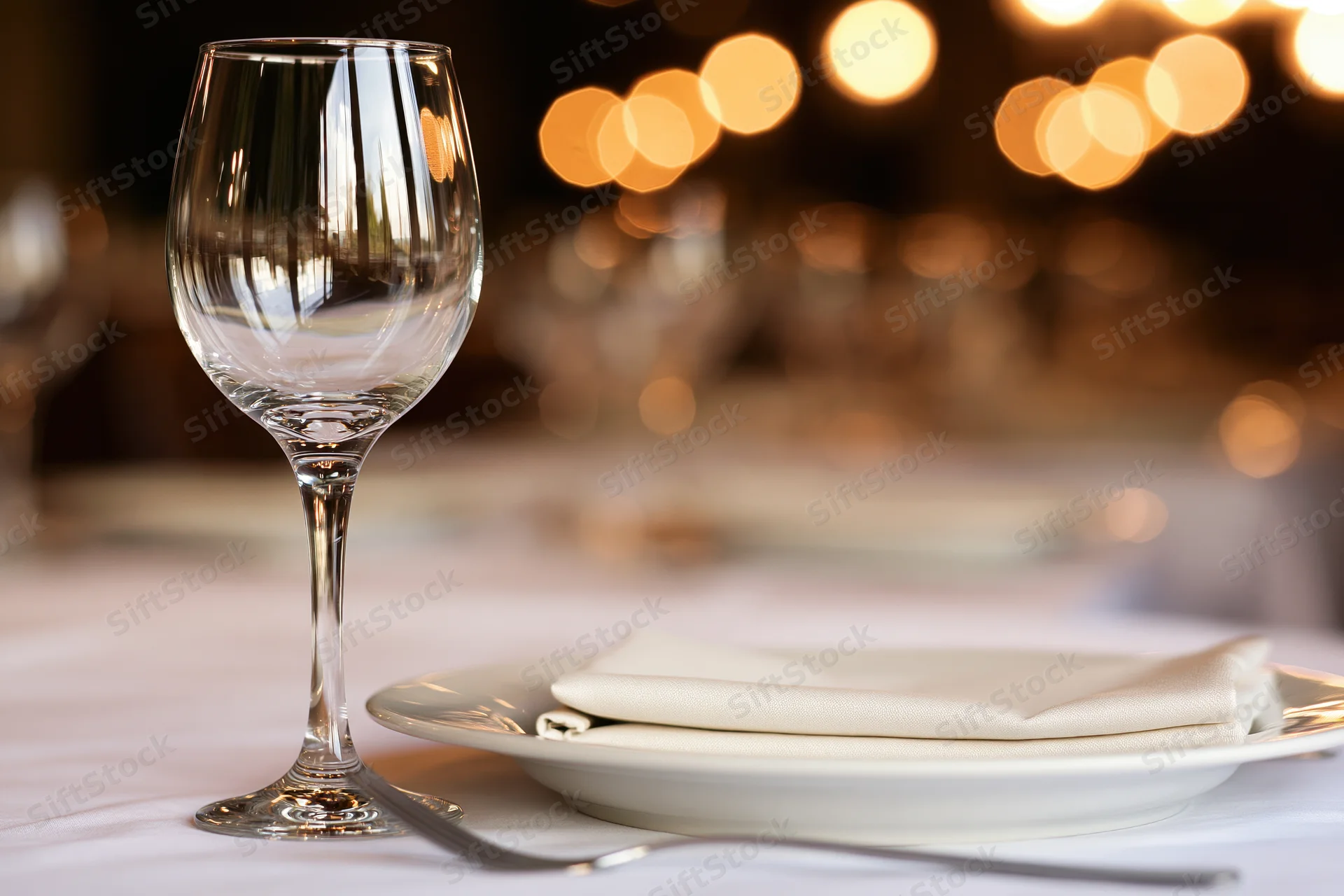 Empty wine glass beside white plate with folded linen napkin on formal dinner table
