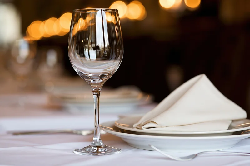 Empty wine glass beside white plate with folded linen napkin on set dining table