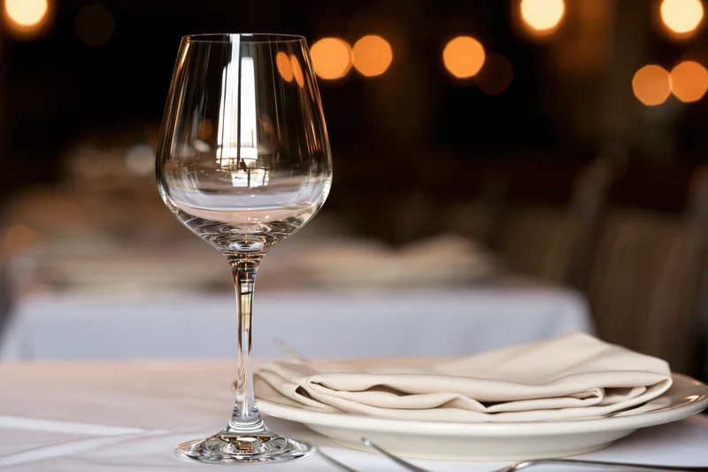 Empty wine glass beside white plate with folded linen napkin on restaurant table