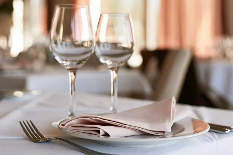Empty wine glasses and folded napkin on white plate at formal dining table