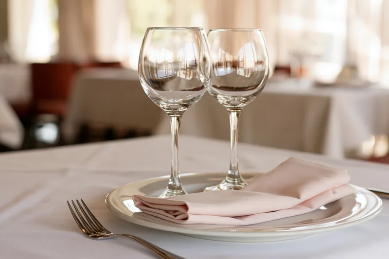 Two empty wine glasses and a folded linen napkin on a white plate at a set dining table