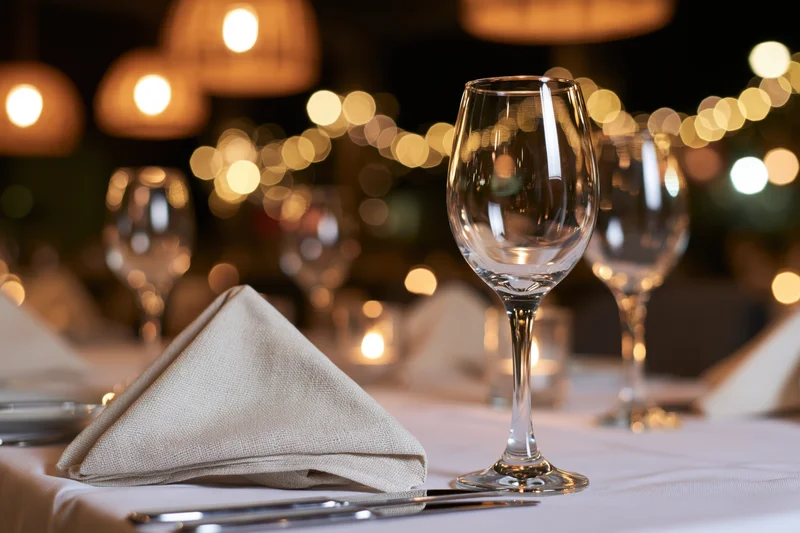 Formally set dinner table with wine glasses and folded linen napkins under warm ambient lighting
