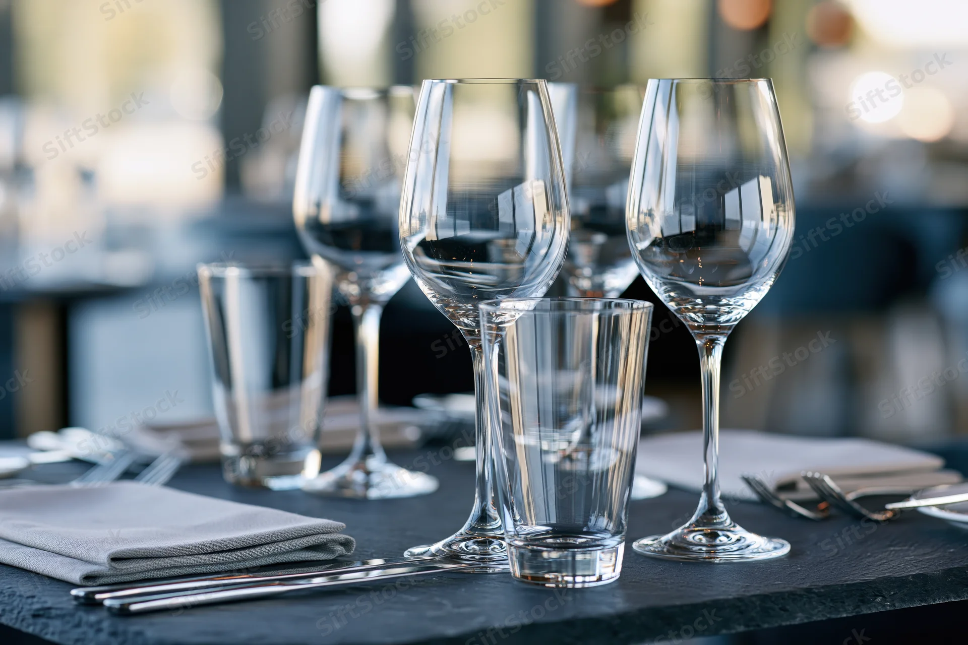 Empty wine glasses and tumblers arranged on a dark restaurant table with cutlery and napkins