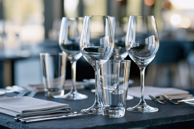 Empty wine glasses and tumblers arranged on a dark restaurant table with cutlery and napkins