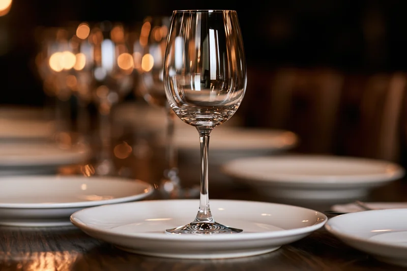 Empty wine glass on white plate set on wooden table with blurred background lights