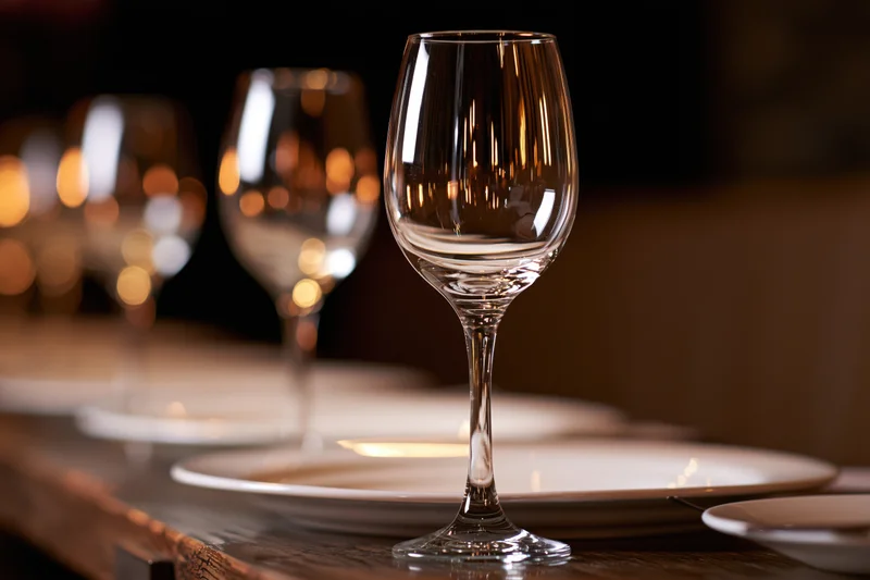 Empty wine glasses and white plates arranged along a wooden table in a dimly lit dining setting