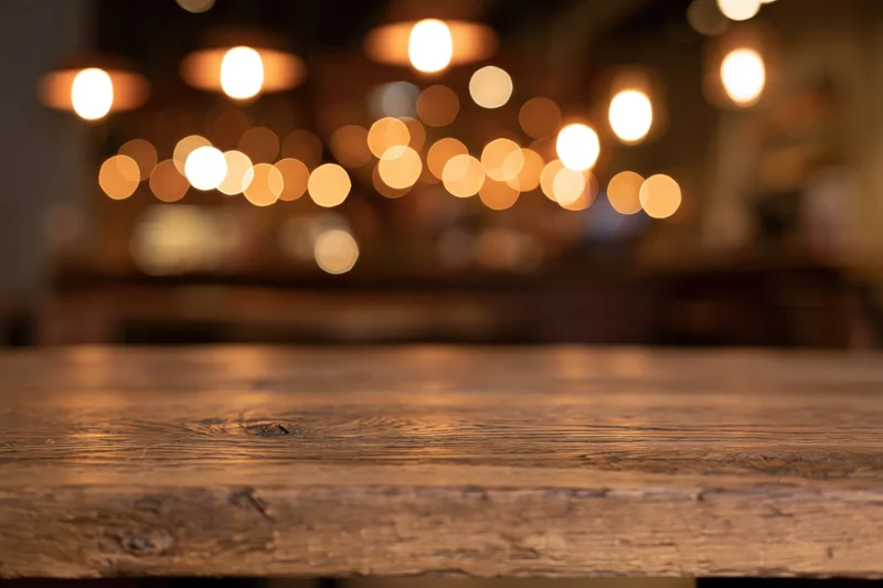 Empty wooden table surface in sharp focus with blurred cafe lights in background