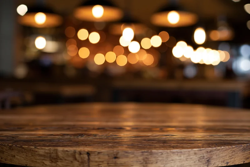 Empty wooden table surface in sharp focus with warm bokeh lights in background