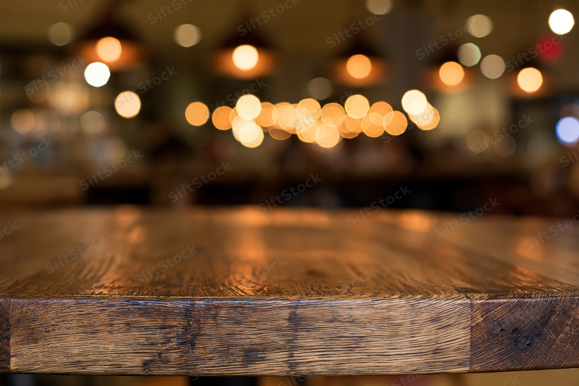 Wooden table surface in sharp focus with blurred restaurant lights in background