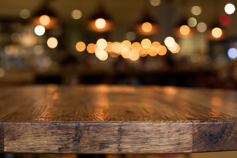Wooden table surface in sharp focus with blurred restaurant lights in background