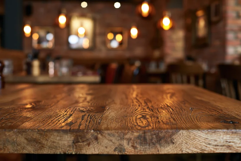 Wooden table surface in focus with blurred restaurant interior behind