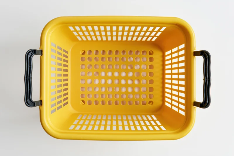 Empty yellow plastic shopping basket with black handles viewed from above on white background