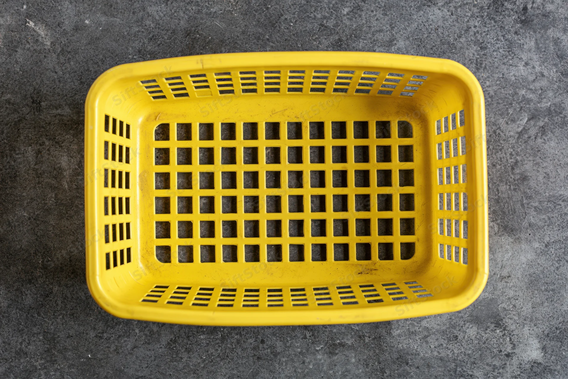 Empty yellow plastic shopping basket viewed from directly above on dark textured surface