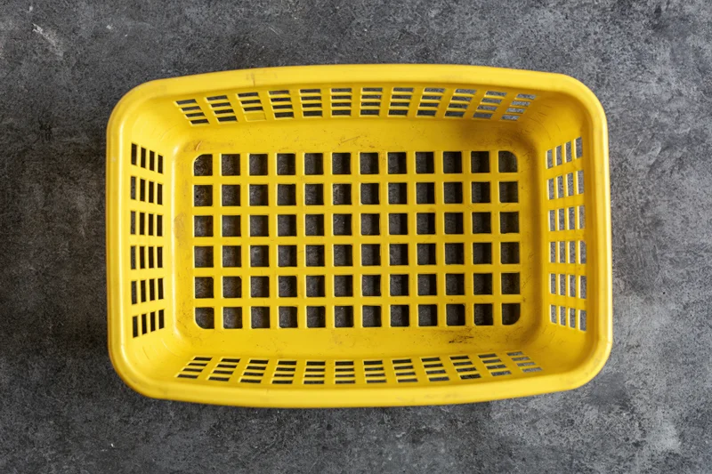 Empty yellow plastic shopping basket viewed from directly above on dark textured surface