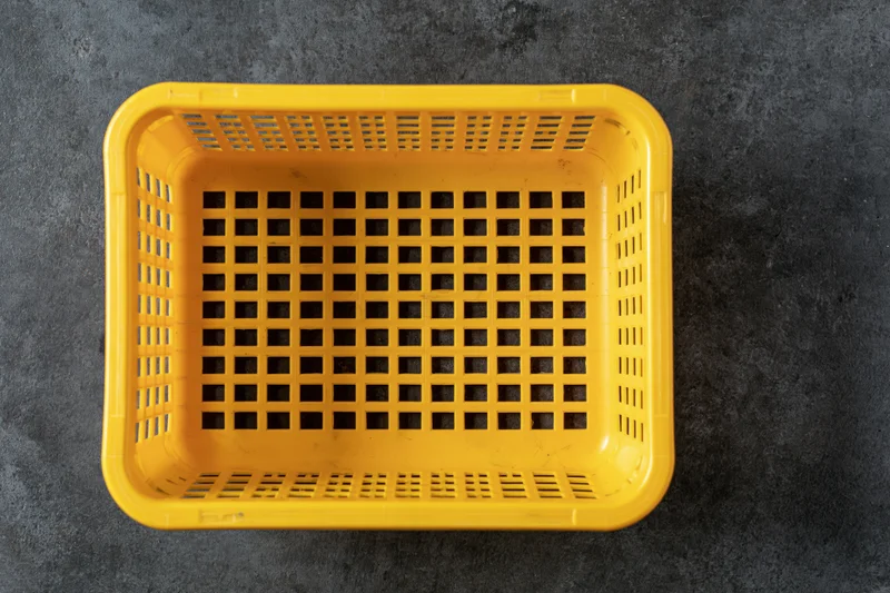 Empty yellow plastic shopping basket viewed from directly above on dark textured surface