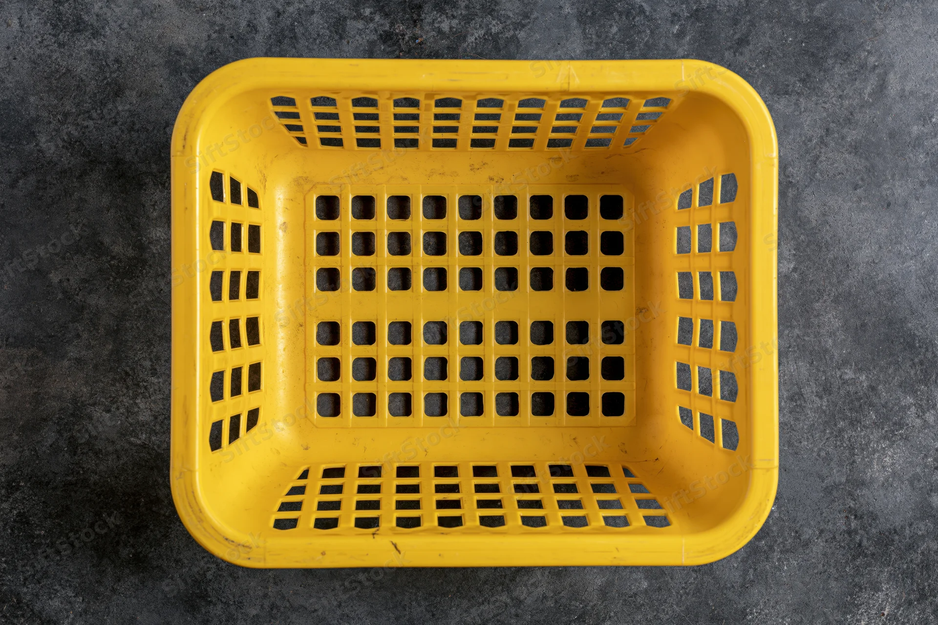 Empty yellow plastic shopping basket viewed from directly above on dark textured surface