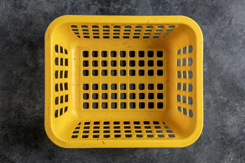 Empty yellow plastic shopping basket viewed from directly above on dark textured surface