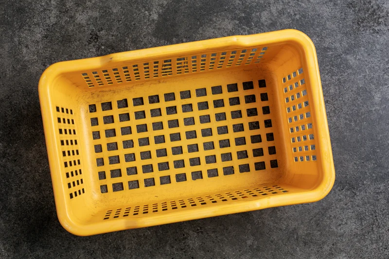 Empty yellow plastic shopping basket viewed from above on dark textured surface