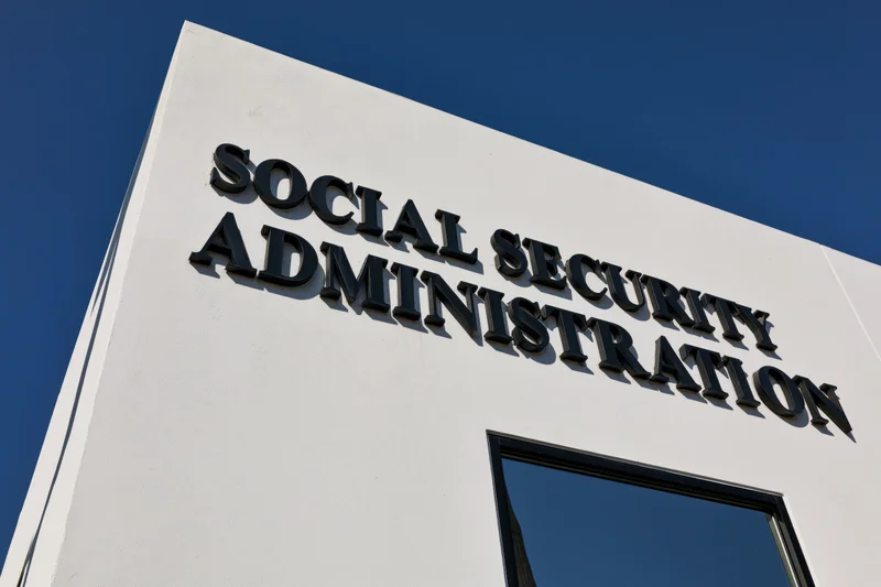 Exterior corner of a government office building with bold black lettering reading social security administration against a clear blue sky