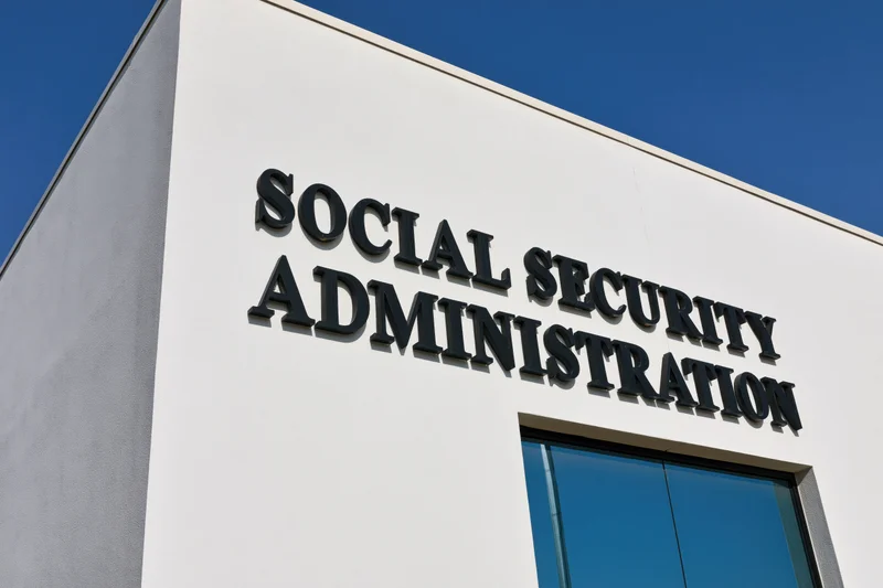 Exterior corner of a government office building with bold black lettering reading social security administration under a clear blue sky
