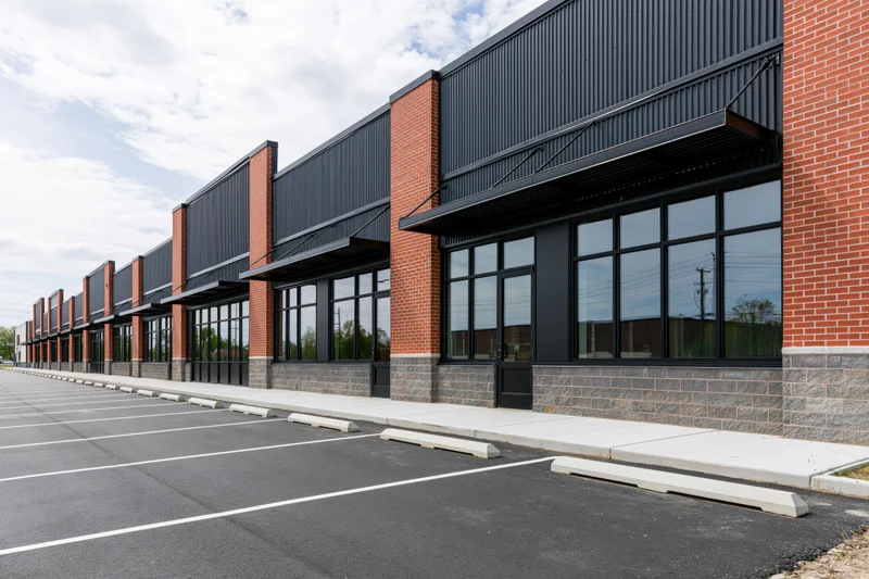 Exterior facade of a newly built suburban retail strip center with brick and metal siding, large glass windows, and an empty asphalt parking lot