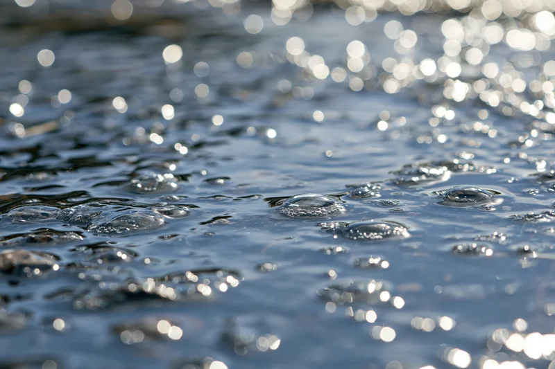 Rain droplets creating ripples and shimmering reflections on a wet surface