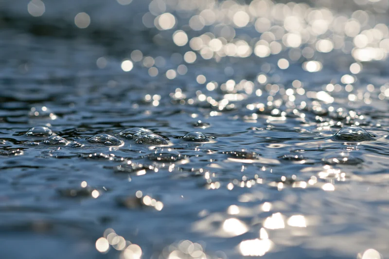 Close-up of water droplets and ripples on a sunlit surface with sparkling reflections and bokeh background