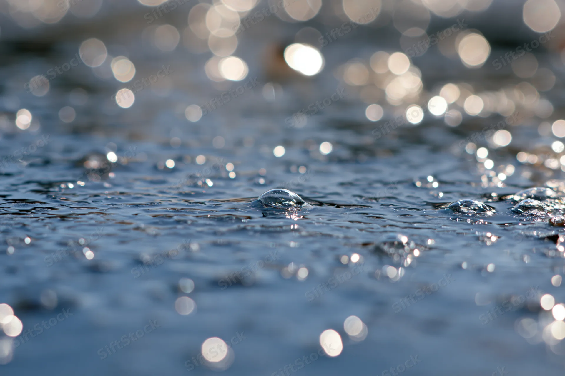 Close-up of water droplets on a rippling surface with sun reflections and bokeh background