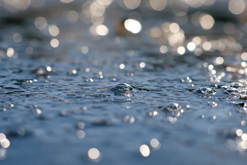 Close-up of water droplets on a rippling surface with sun reflections and bokeh background