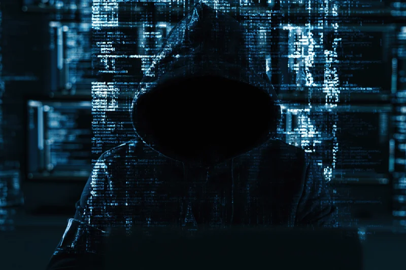 Hooded figure sitting in darkness with digital code overlay on screen