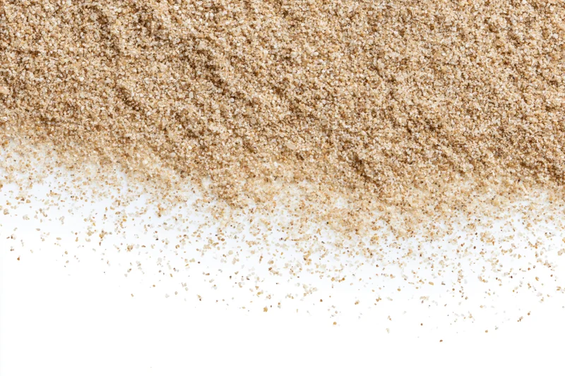 Fine beach sand scattered across a clean white surface forming a textured pile with copyspace below