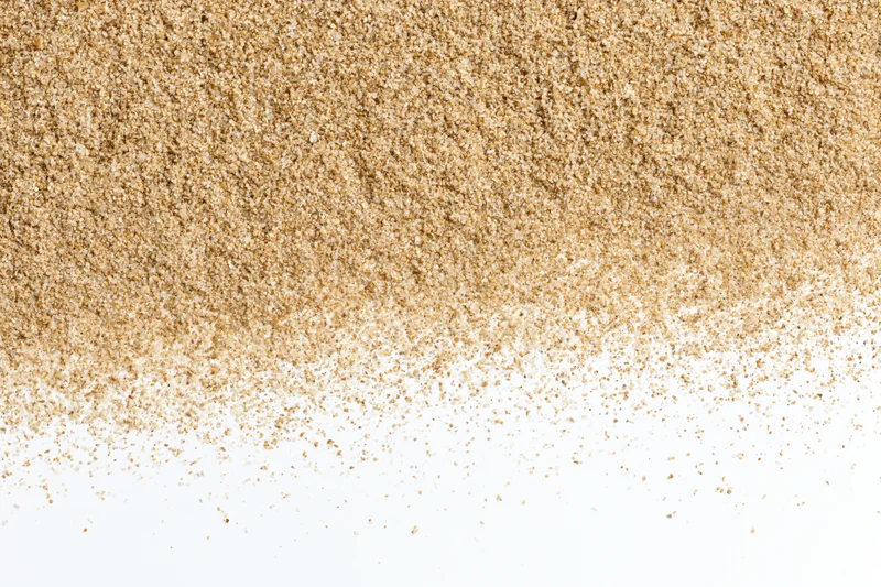 Fine beach sand scattered across a white surface forming a textured pile with copyspace below
