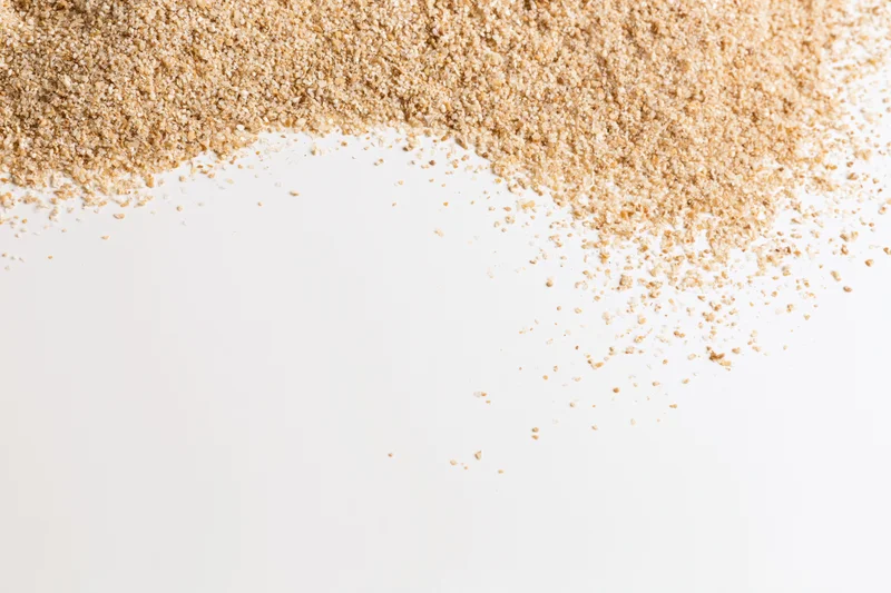 Fine dry beach sand scattered across the upper-left corner of a white surface