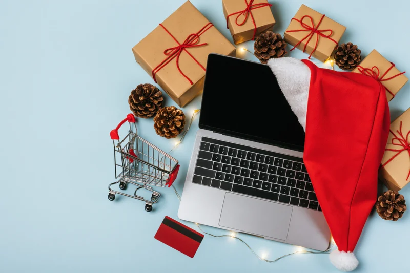 Laptop with santa hat and gifts arranged for online christmas shopping on blue background