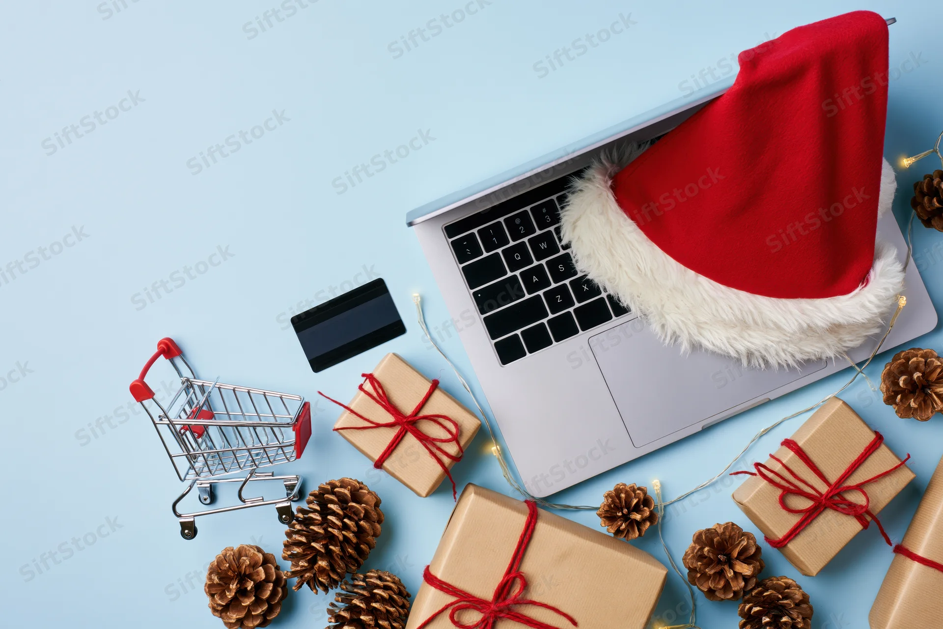 Laptop with santa hat and holiday gifts arranged on blue surface